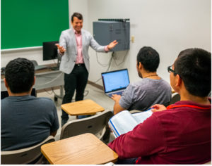 A teach talking to three students in a classroom.