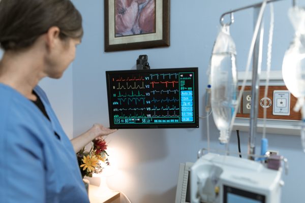 A medical worker checking vitals alongside a hospital bed.